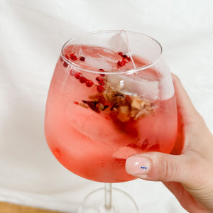 A hand holding a balloon glass of pink Gin & Tonic 