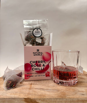 Packaging of 'Cherry, Rose & Chilli' infusion bags for gin with a glass of red liquid on a wooden surface.
