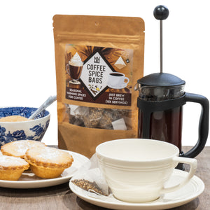 Coffee spice bags with a cup, saucer, and pastries on a table.