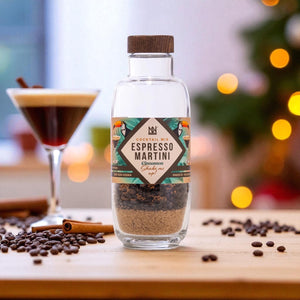 Bottle of Espresso Martini Cinnamon flavour cocktail mix with a glass of cocktail and coffee beans on a wooden surface.