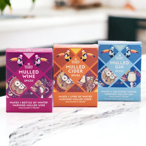 Three packaged mulling spice blends from Natural & Noble, each designed for making mulled wine, cider, and gin. The packages are colorful and illustrate the contents and instructions for use.