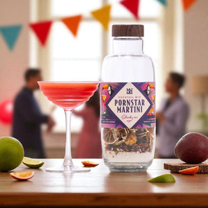 Bottle of Pornstar Martini cocktail mixer with a cocktail and fruit on a table.