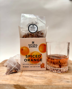 Spiced orange infusion bags for gin with a glass of gin on a wooden surface.