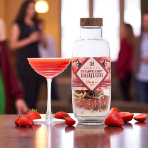 Strawberry Daiquiri cocktail mix bottle with a glass of strawberry daiquiri and fresh strawberries on a table.