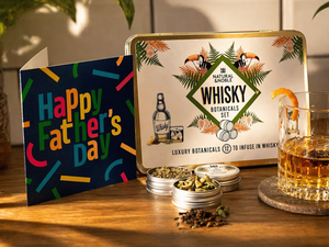 Glass of Whisky, alongside Natural & Noble DIY Whisky Kit, Open Tins of Botanicals and Fathers day Card